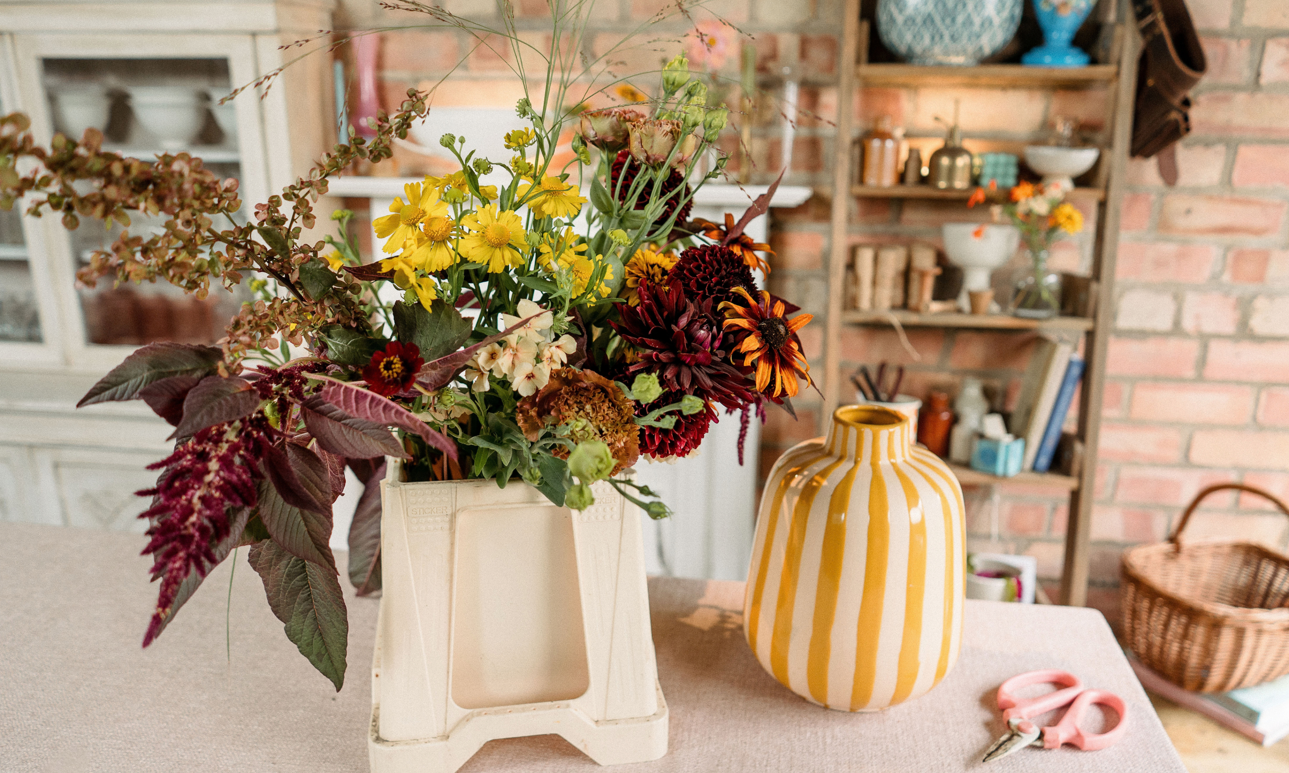Autumnal flowers in bucket next to yellow striped vase
