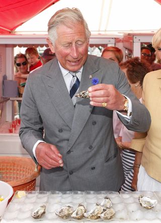 King Charles wearing a gray suit eating an oyster at a market