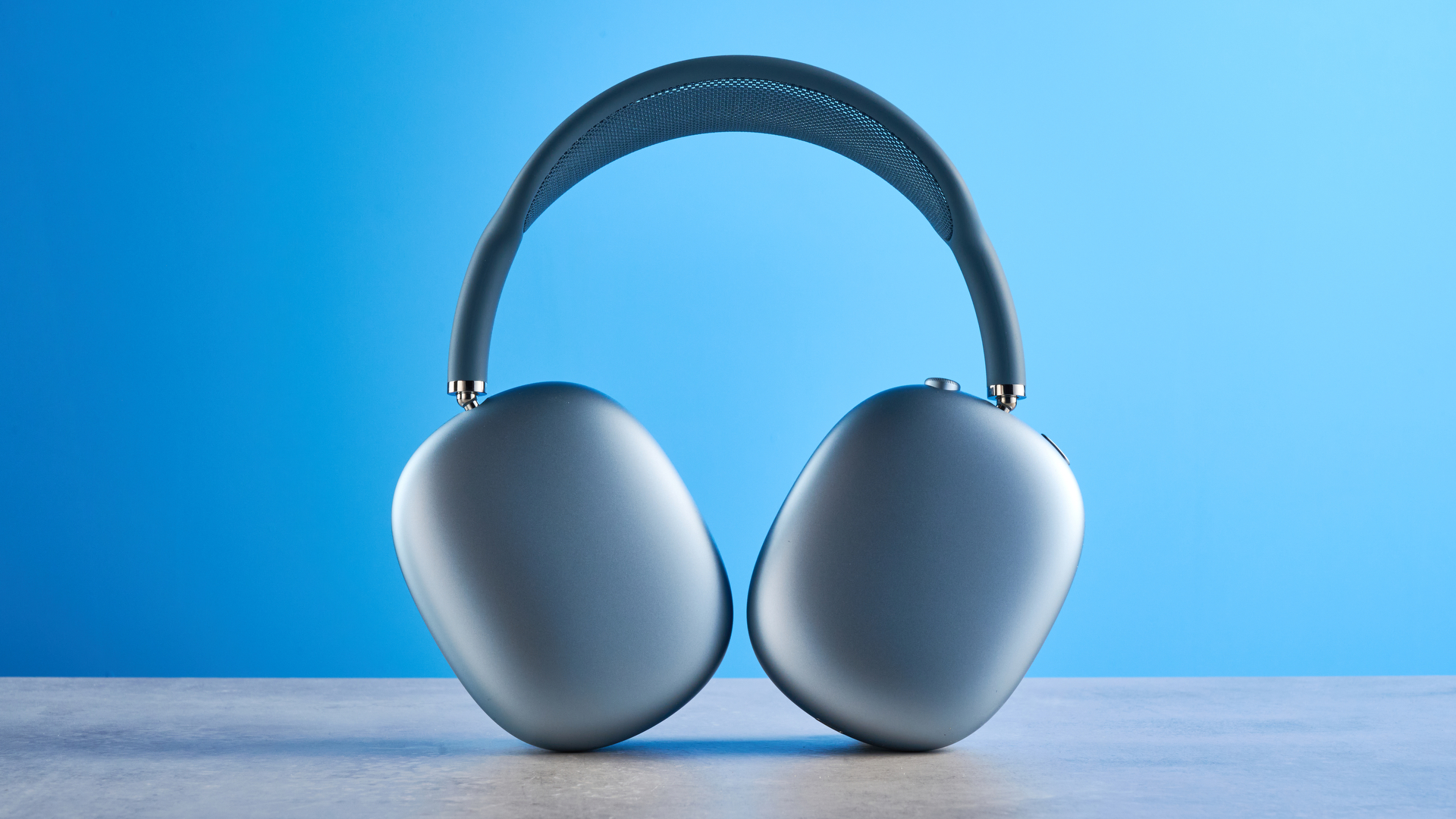 the apple airpods max 2 in blue photographed against a blue tom's guide background, showing the mesh headband, anodized aluminum ear cups, carry case, and controls