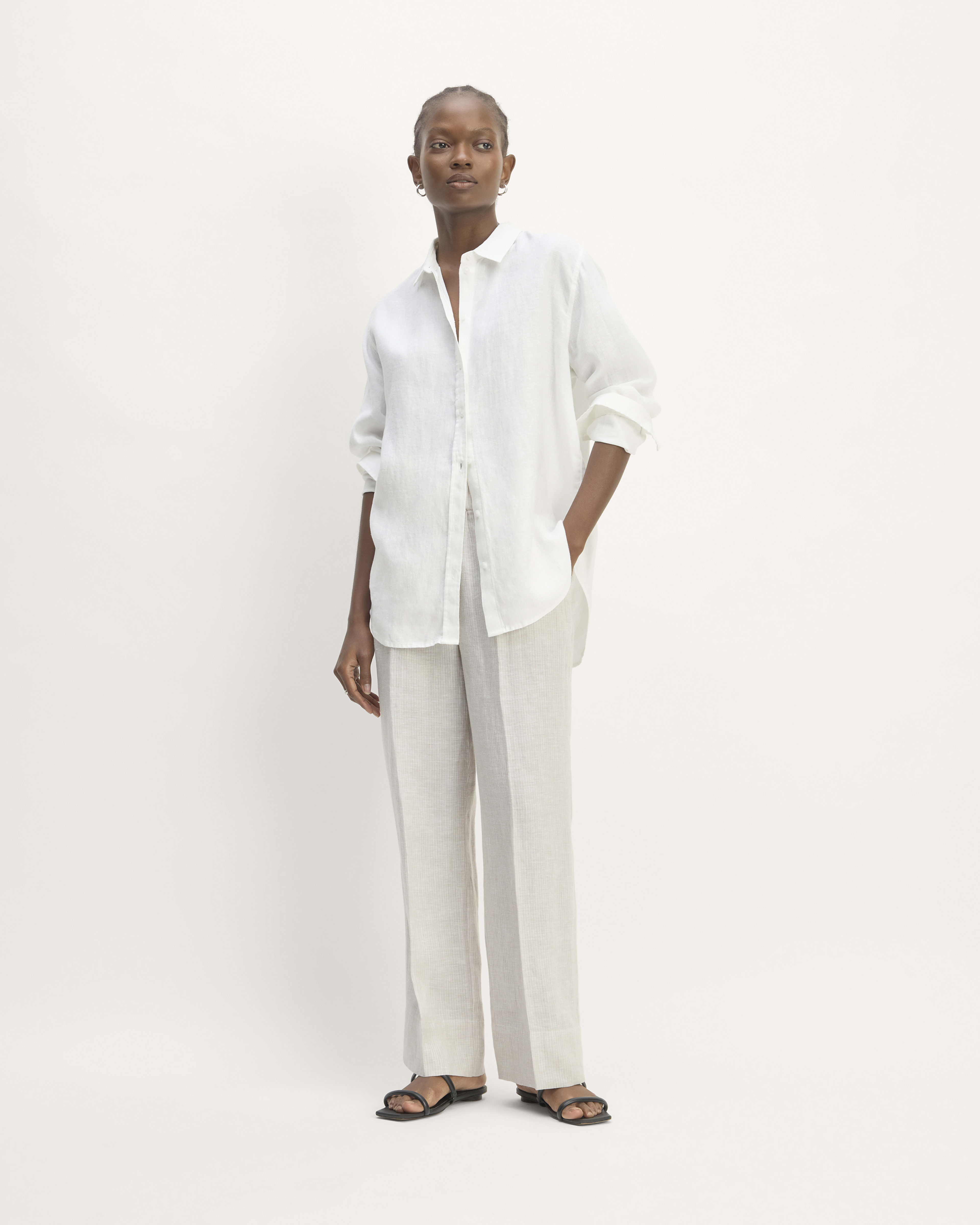 a model wears a white button-down shirt with off-white trousers