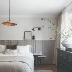 A neutral living room with half of the wall covered in a quilted padding in grey, with a black adjustable wall light and a rattan pendant light
