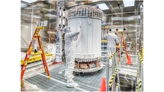 Technicians in white protective suits work on a delicate science instrument