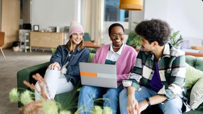 Three Gen Z friends on a sofa smiling and talking with one another.