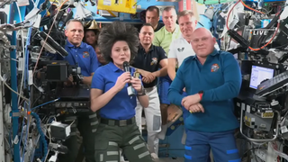 group of astronauts and cosmonauts assembled in the international space station. samantha cristoforetti is in the front holding a mic
