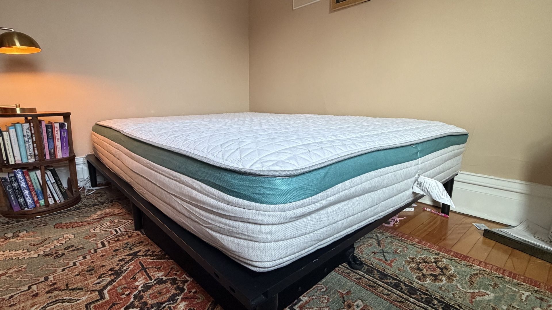 The image shows a white mattress with green trim placed on a black metal bed foundation and placed within a bedroom