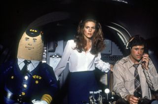 Julie Hagerty as Elaine Dickinson and Robert Hays as Ted Striker in a cockpit with the inflatable autopilot "Otto" on the left in Airplane!