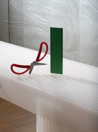 A red pair of scissors and a green aluminium pen rest from the ‘Components’ series by Mario Tsai are displayed on a ‘Grid’ bench