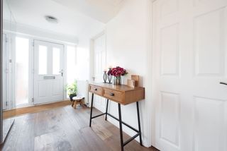 A white modern hallway with a coir matt and wooden console table opposite a mirror