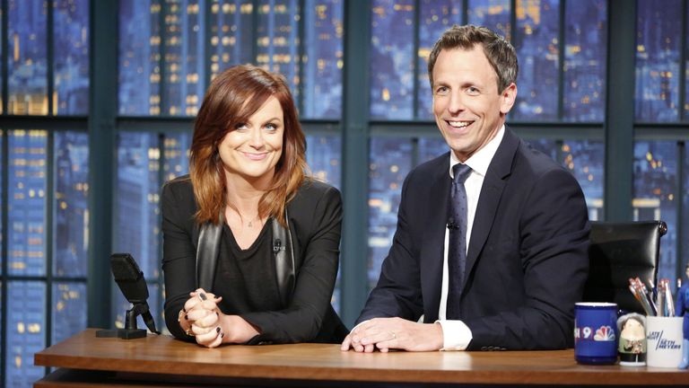 Amy Poehler and Seth Meyers sat behind a desk at a talk show.