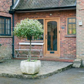 red brick home with wooden door and chair border and white bench