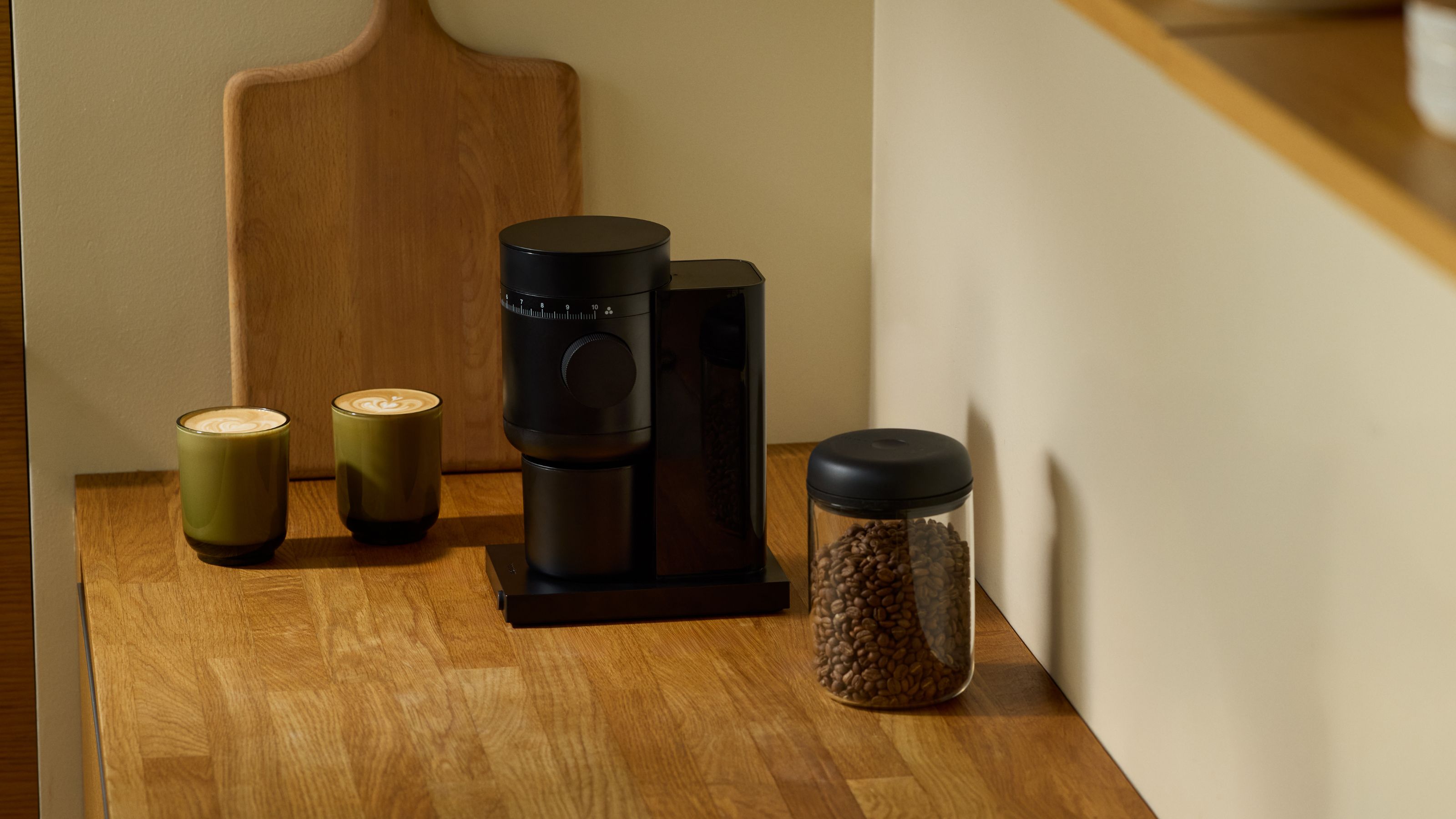 A Fellow Conical Burr Coffee Grinder on a wooden kitchen counter, with a two mugs of coffee beside it. 