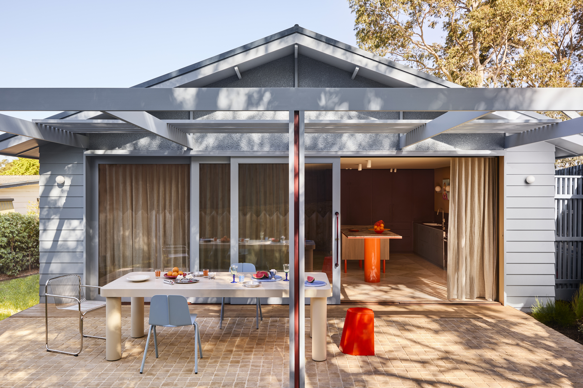 a blue weatherboard home's outdoor dining area with brick paving and a pergola