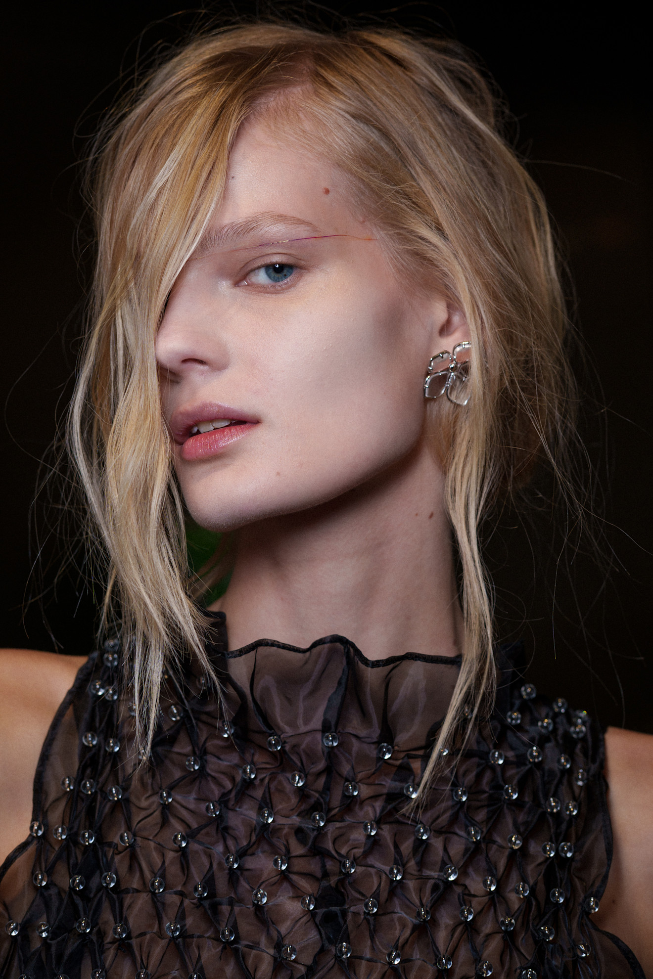 A model at Susan Fang SS26 show with dishevelled hair in front of her face and a fine holographic ribbon across both her upper eyes