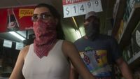 A woman with a red bandana over her face wearing sunglasses walking in front of a man with a bandana over his face and a trucker hat one in GTA: VI