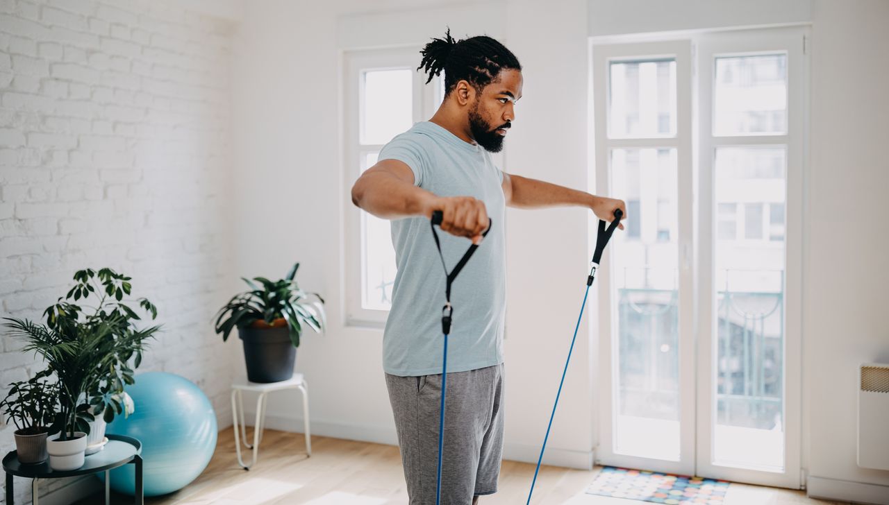 Man performing lateral raise exercise at home using a resistance band with handles