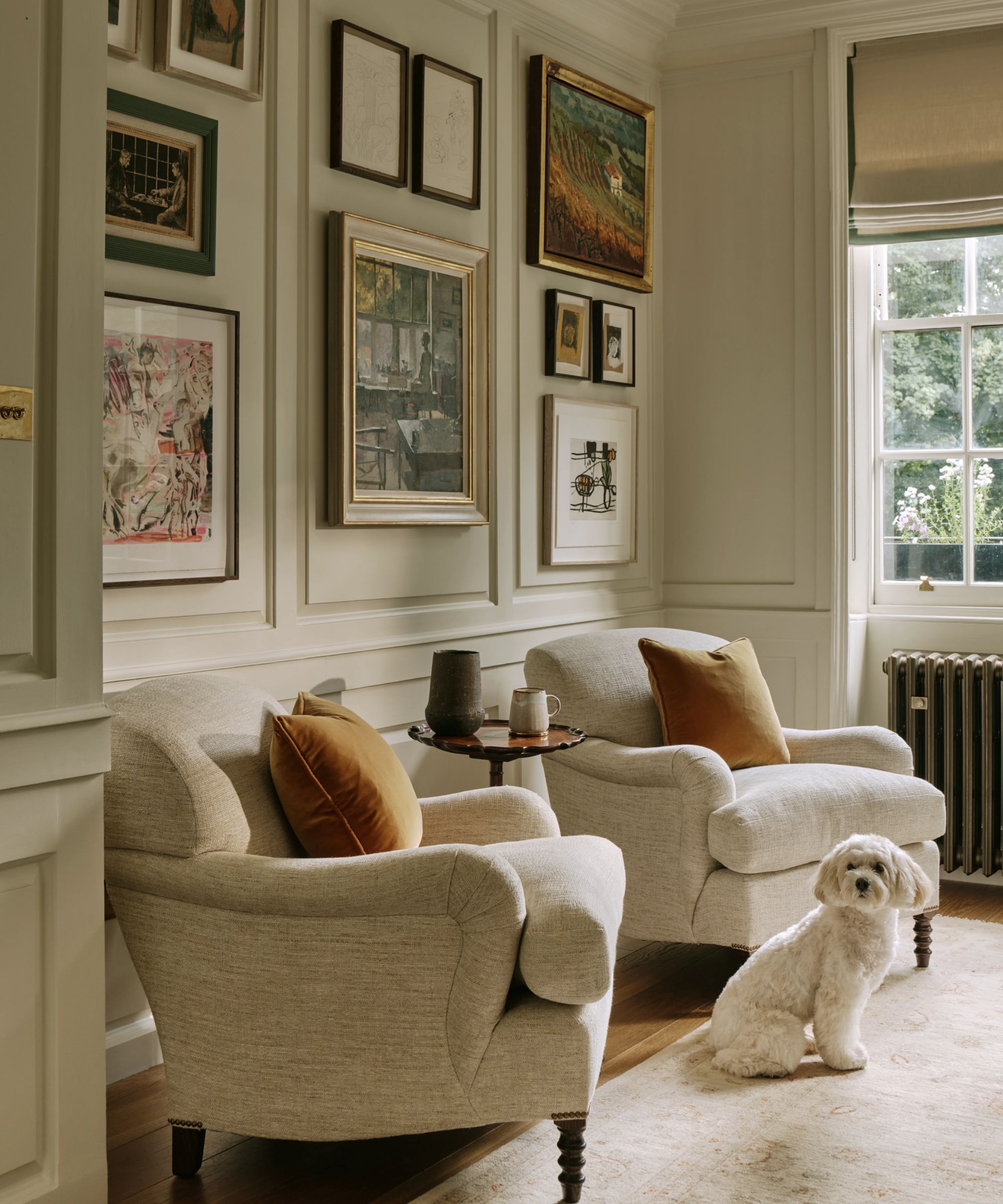a traditional sitting area in a dining room with wall moldings, a gallery wall, two armchairs and a small white dog sitting on a rug