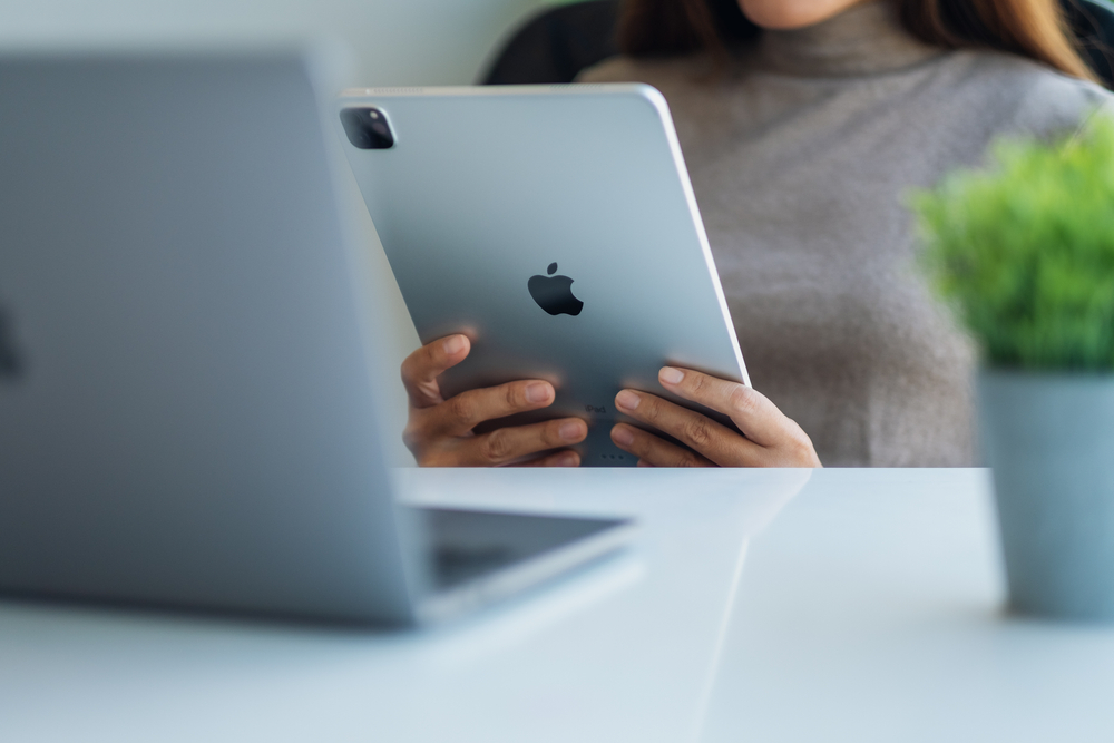 A person holding an iPad near a MacBook