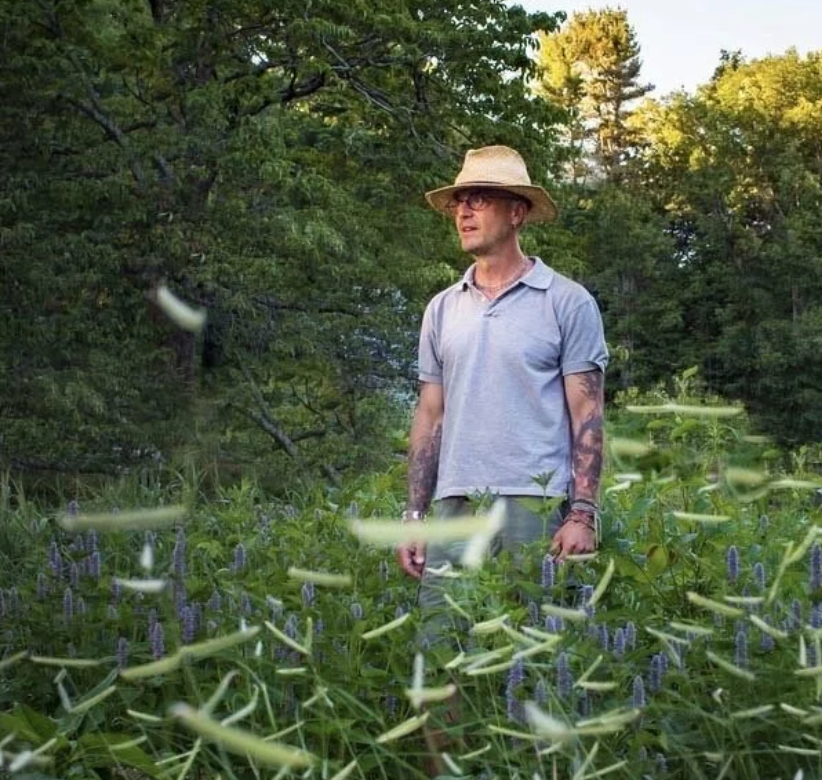 man wearing a blue top and hat standing in a garden