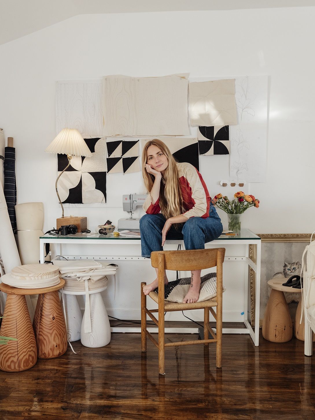 A young girl dressed in a cream and red sweatshirt and denim jeans sits on a white desk next to her plump, fun furniture pieces and a softly warm table lamp.