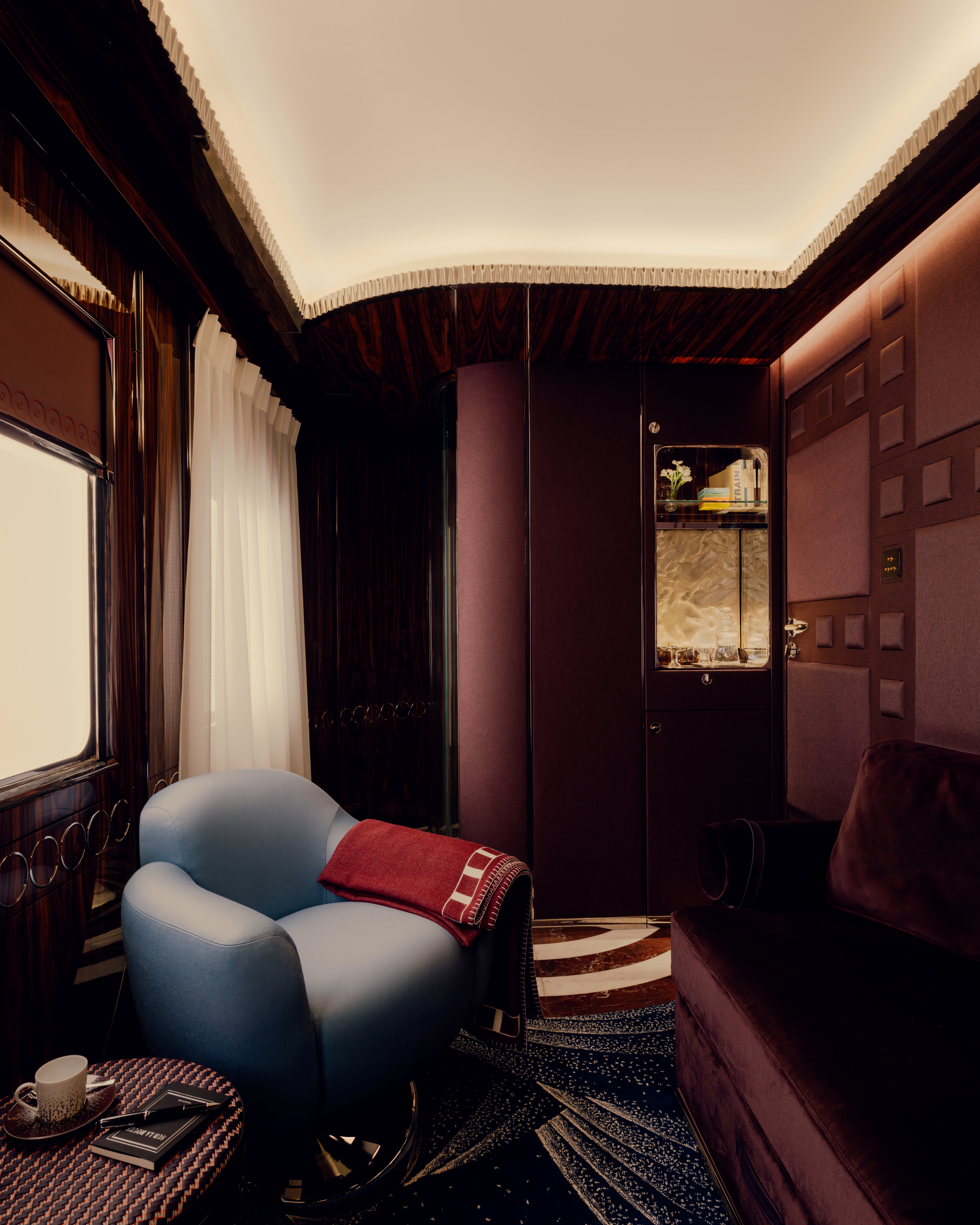 A series of images showcasing the vintage-inspired interiors of a luxury train, characterized by lacquered marquetry, plush textiles, geometrical patterns, and a chocolate, gold, cherry plum, green, and baby blue palette.