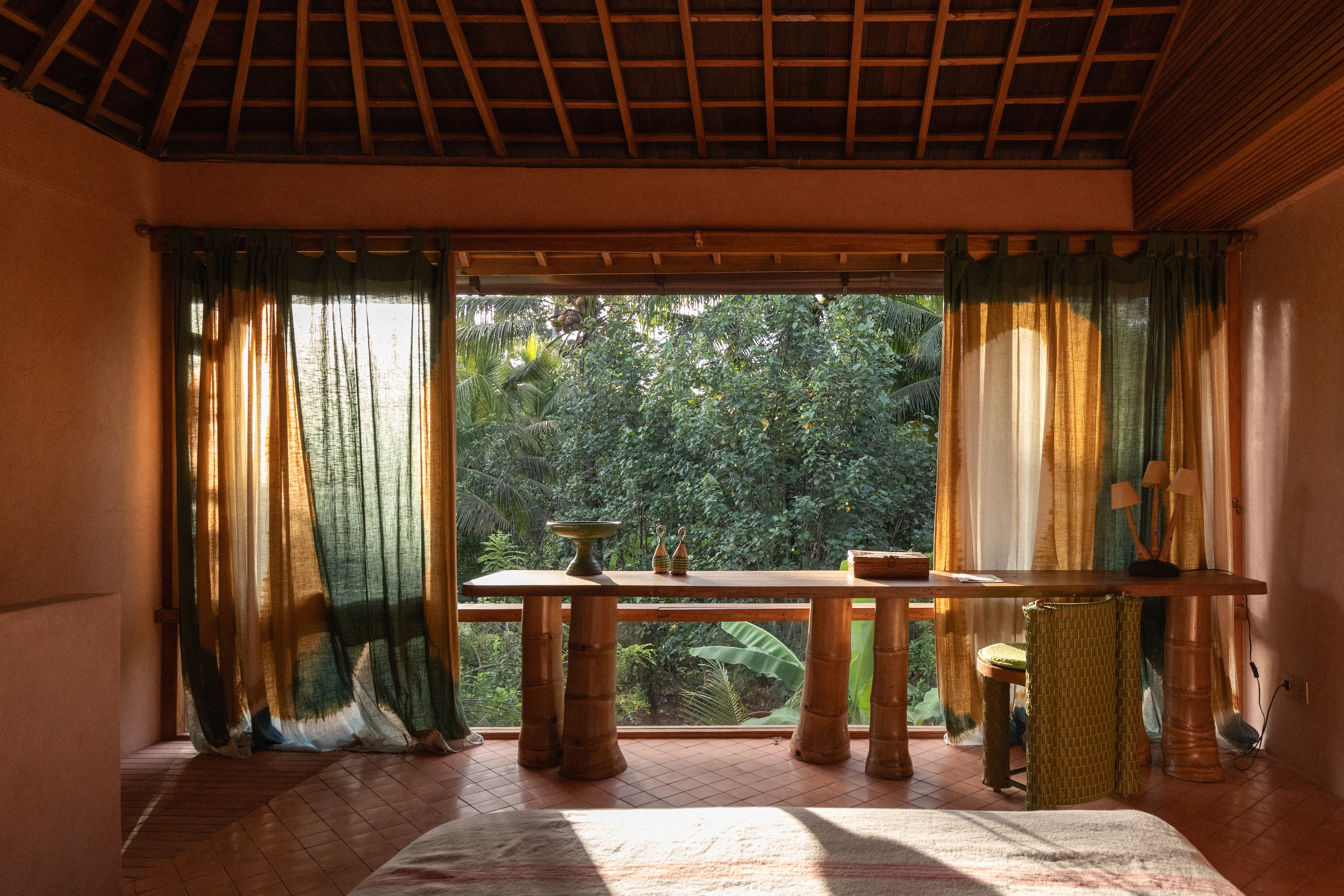 Interiors of a tropical interiors with curved passageways, terracotta walls, colorful curtains, woody furniture, color pops, and nature all around.