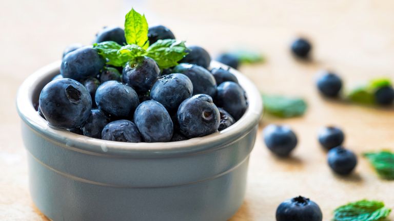 A bowl of blueberries topped with a sprig of mint