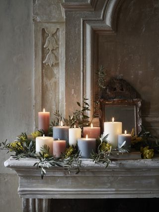 ornate mantel with selection of cream, gray and coral pillar candles with foliage woven inbetween small mirror