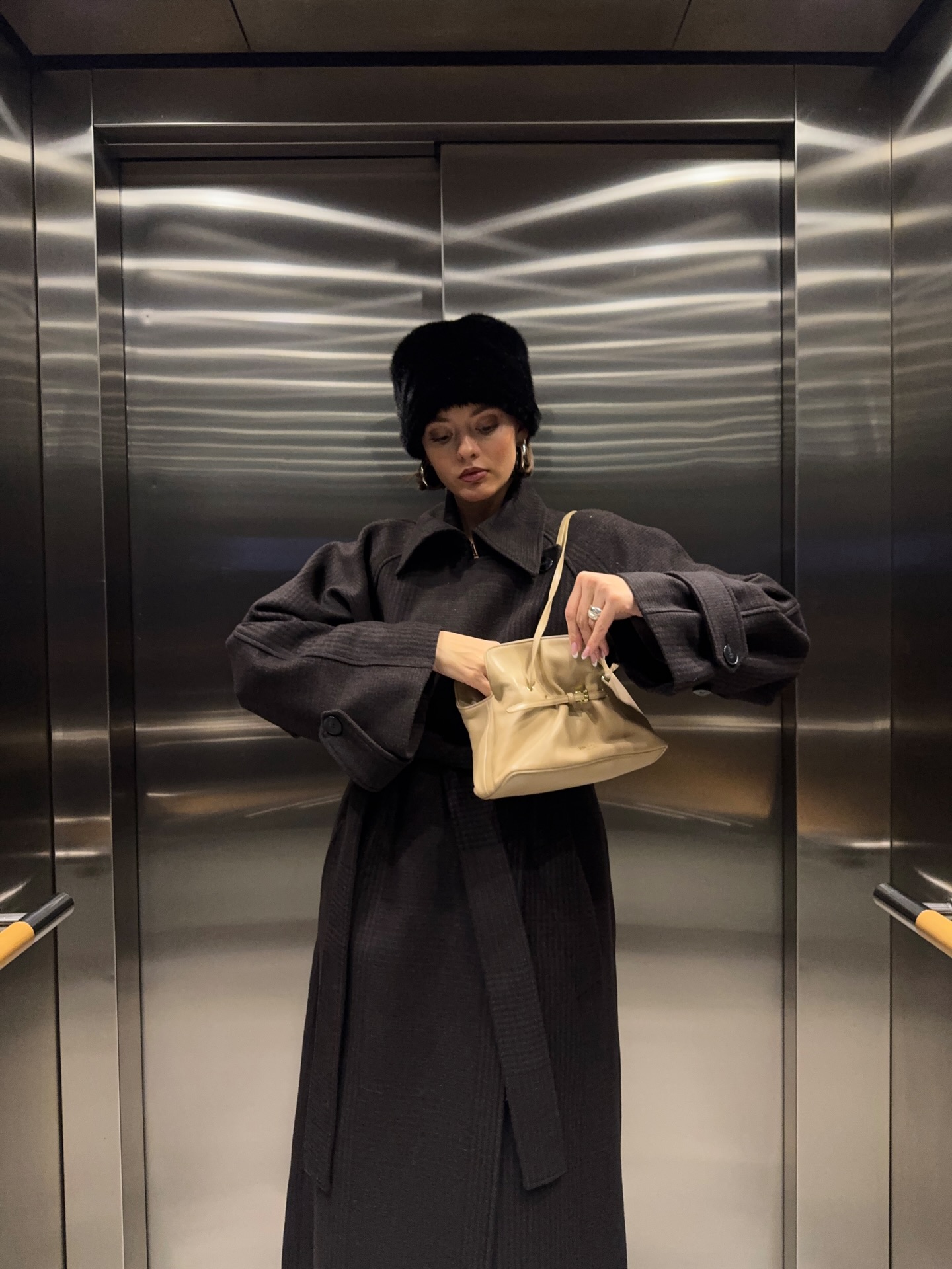 @maryljean is in a long brown belted coat, wearing the faux-fur hat trend