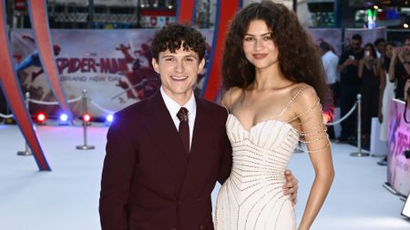 Tom Holland in a black suit and dark tie and Zendaya in a white dress with silver metal trim at the Spider-Man: Brand New Day premiere.