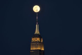 a spire atop a skyscraper overlaps the full moon