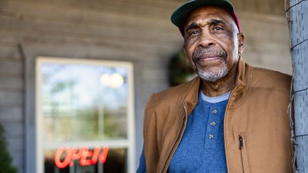 An older business owner stands outside his business.