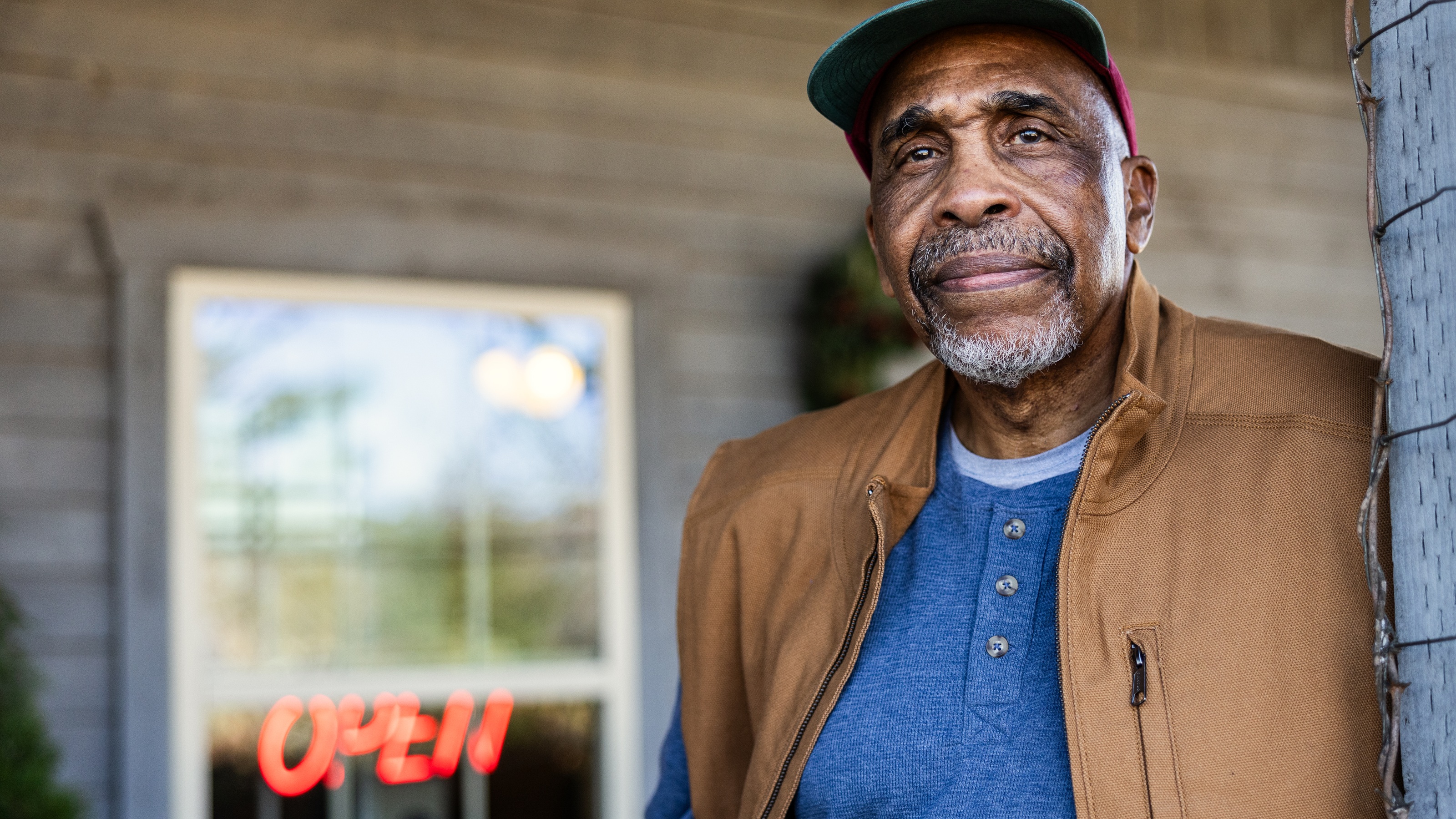 An older business owner stands outside his business.