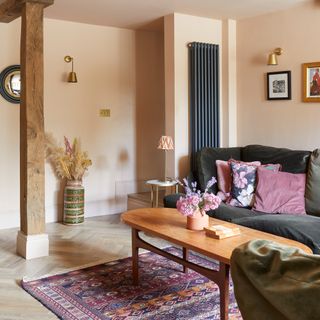 living room with peach walls black velvet sofa with pink and purple cushions and wall hanging vertical radiator