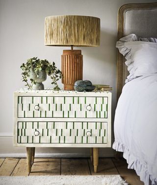 bedroom with bone inlay nightstand in green and cream, upholstered bed with check blanket, gold table lamp, plant, wooden floor