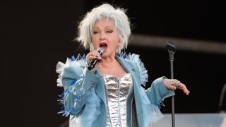 Cyndi Lauper performing at Glastonbury Festival wearing a silver corset, blue blazer and bright pink lipstick