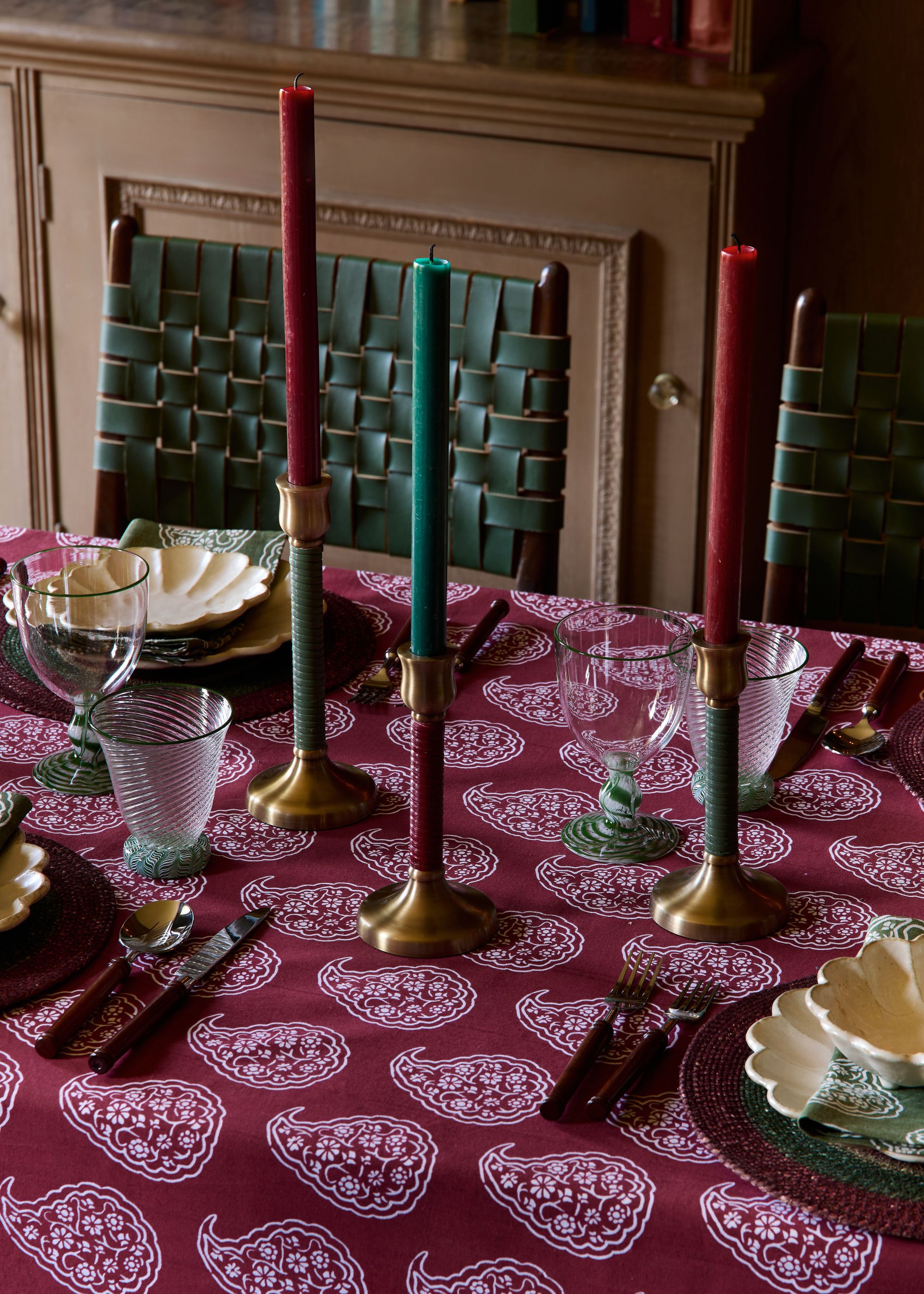 A festive tablescape with a burgundy-patterned tablecloth, red and green taper candles, and scalloped bowls.