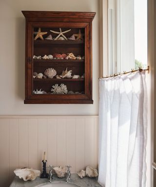 vintage style bathroom with an anqtiue cabinet filled with shells and a cafe curtain