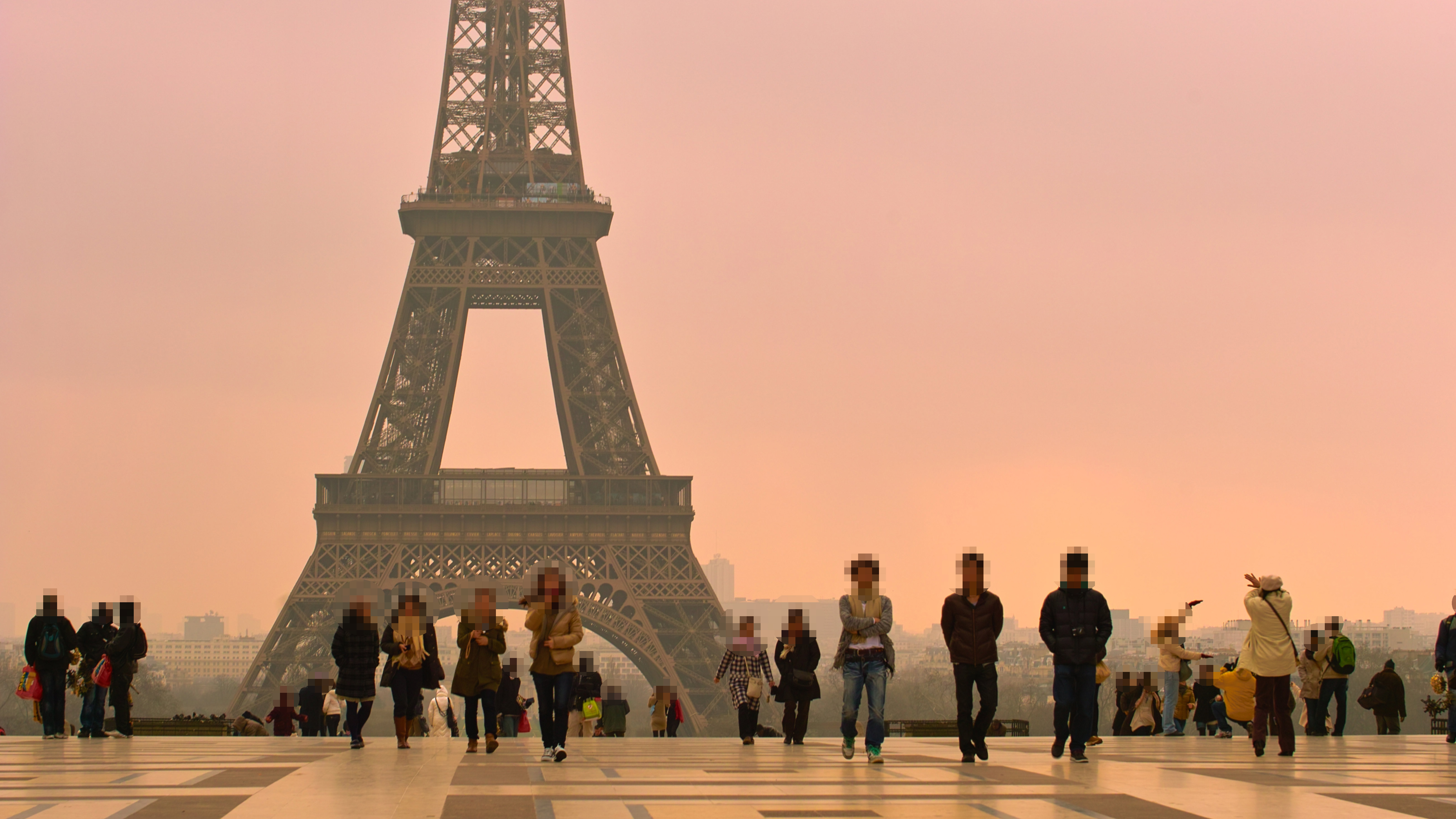 A shot of The Eiffel Tower in Paris in daytime with the faces of pedestrians in the foreground blurred