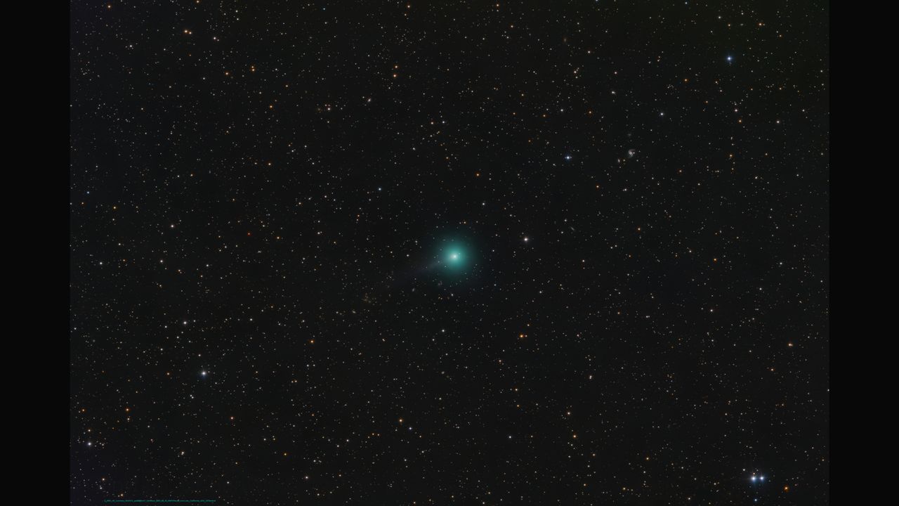 A bright green comet is pictured to the bottom left of a starfield against a black sky, with a long tail extending to the upper right of the screen.