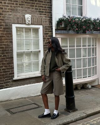 @_livmadeline wears a jacket, knit vest, tailored shorts and loafers with socks