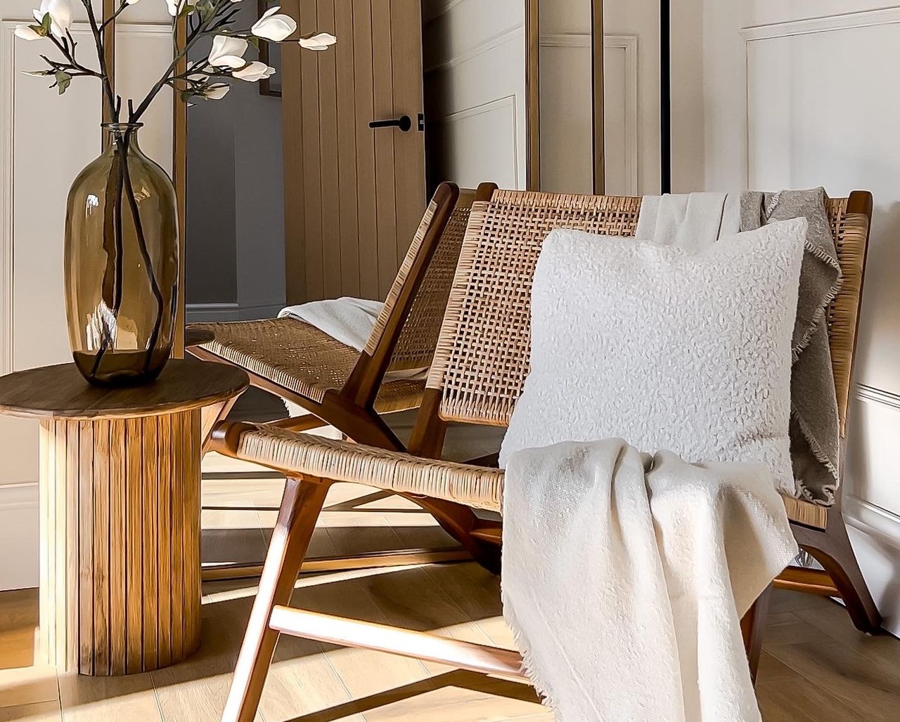 A wicker chair next to a wooden side table decorated with an amber glass vase and magnolia flowers