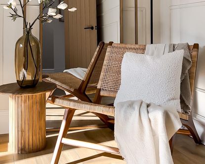 A wicker chair next to a wooden side table decorated with an amber glass vase and magnolia flowers