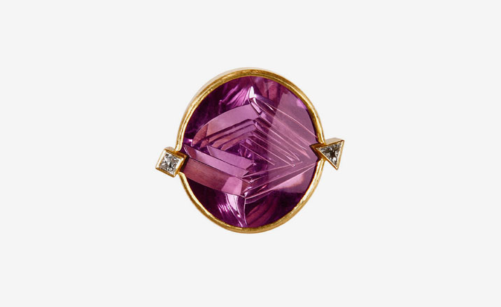 Pink precious stone set into a gold casing with one square and one triangular diamond