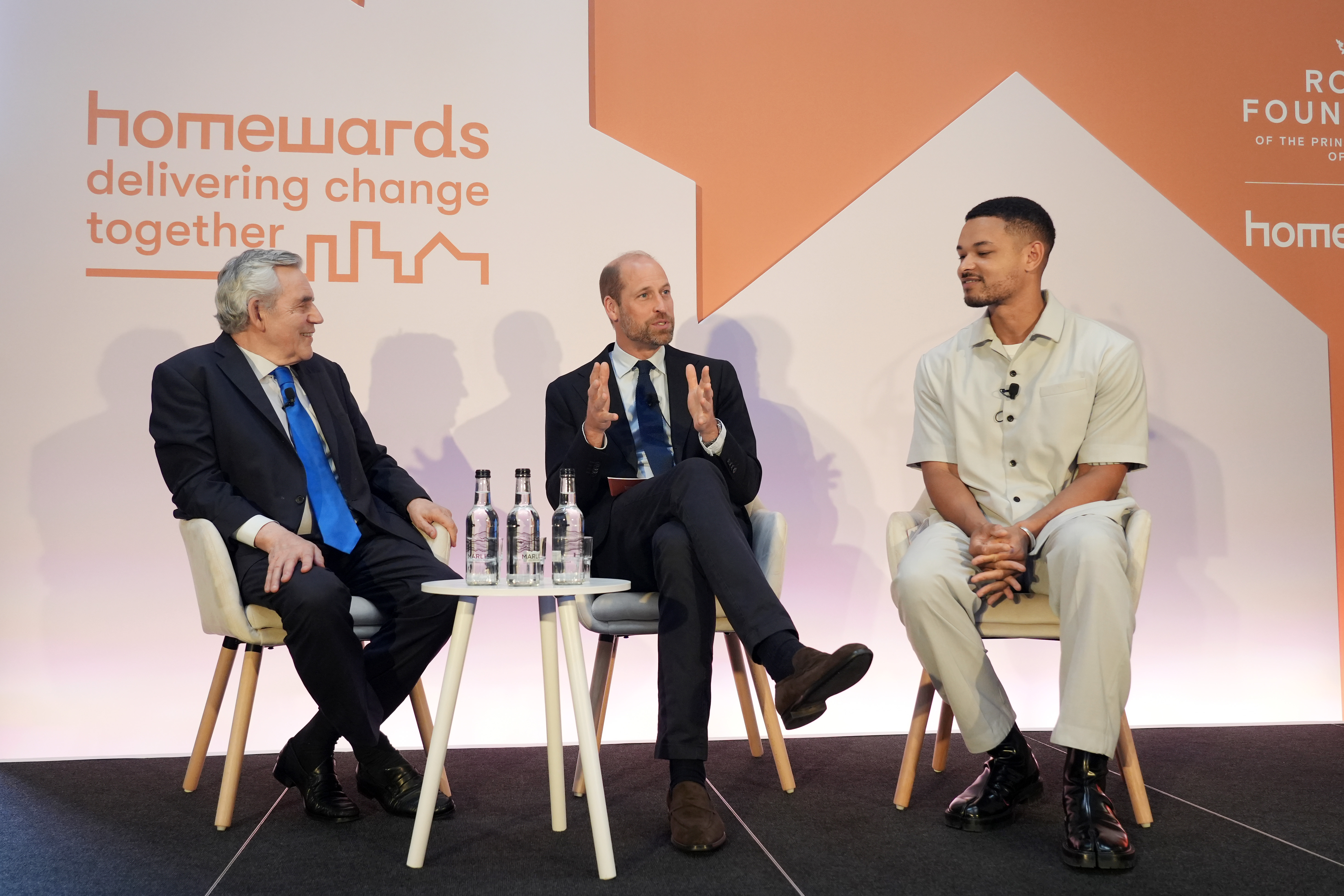 Prince William sitting on stage with two men in front of a Homewards backdrop