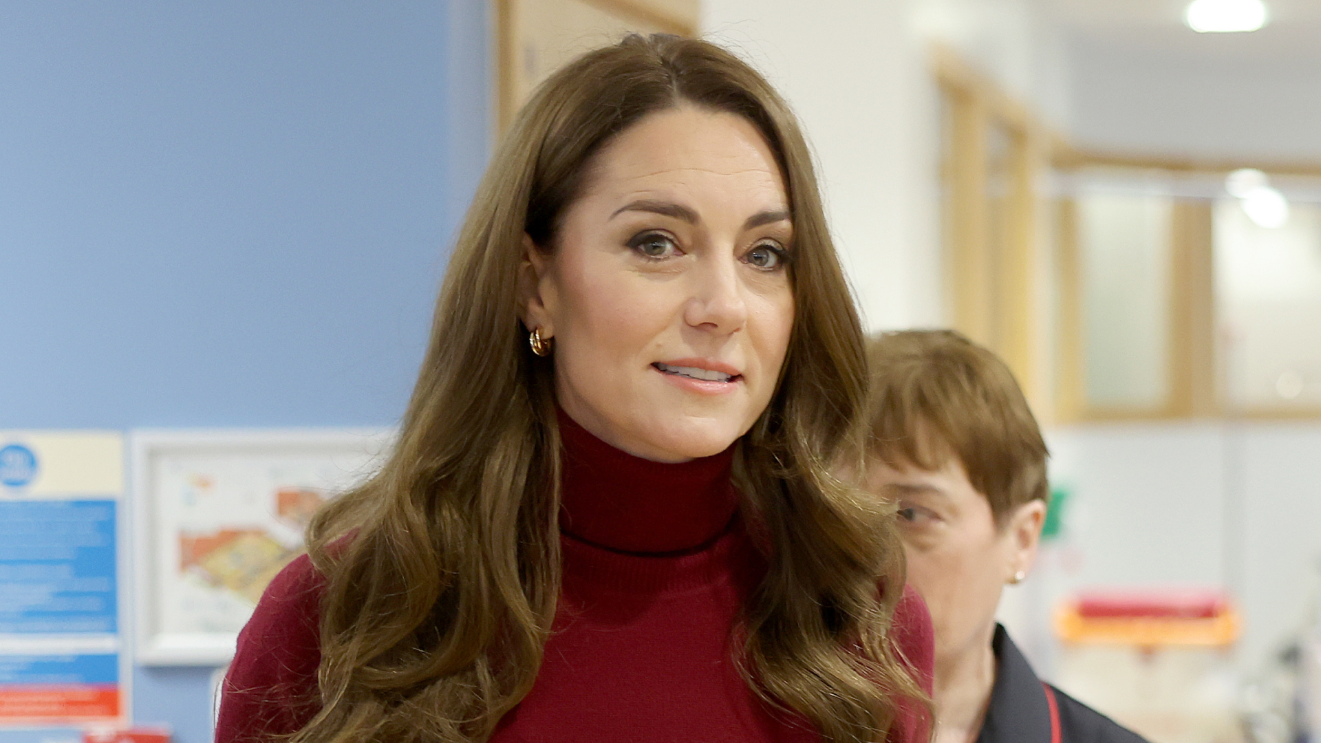 Kate Middleton wears a red polo neck sweater and has long curly brown hair