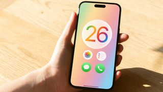 A render of the Apple iOS 26 logo with circular app icons on an iPhone held in a hand.