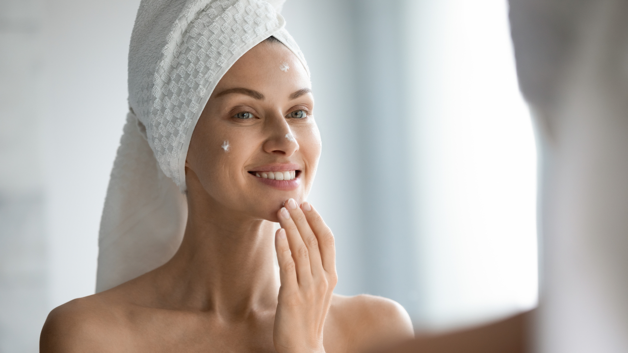 A woman putting lotion on her face in front of a mirror.