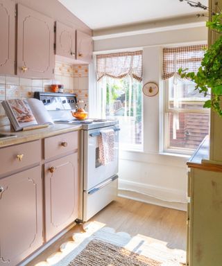 small kitchen with light pink cabinets, gingham curtains and woven rug