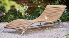 A curved wooden sun lounger on a gravelled patio