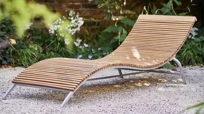 A curved wooden sun lounger on a gravelled patio